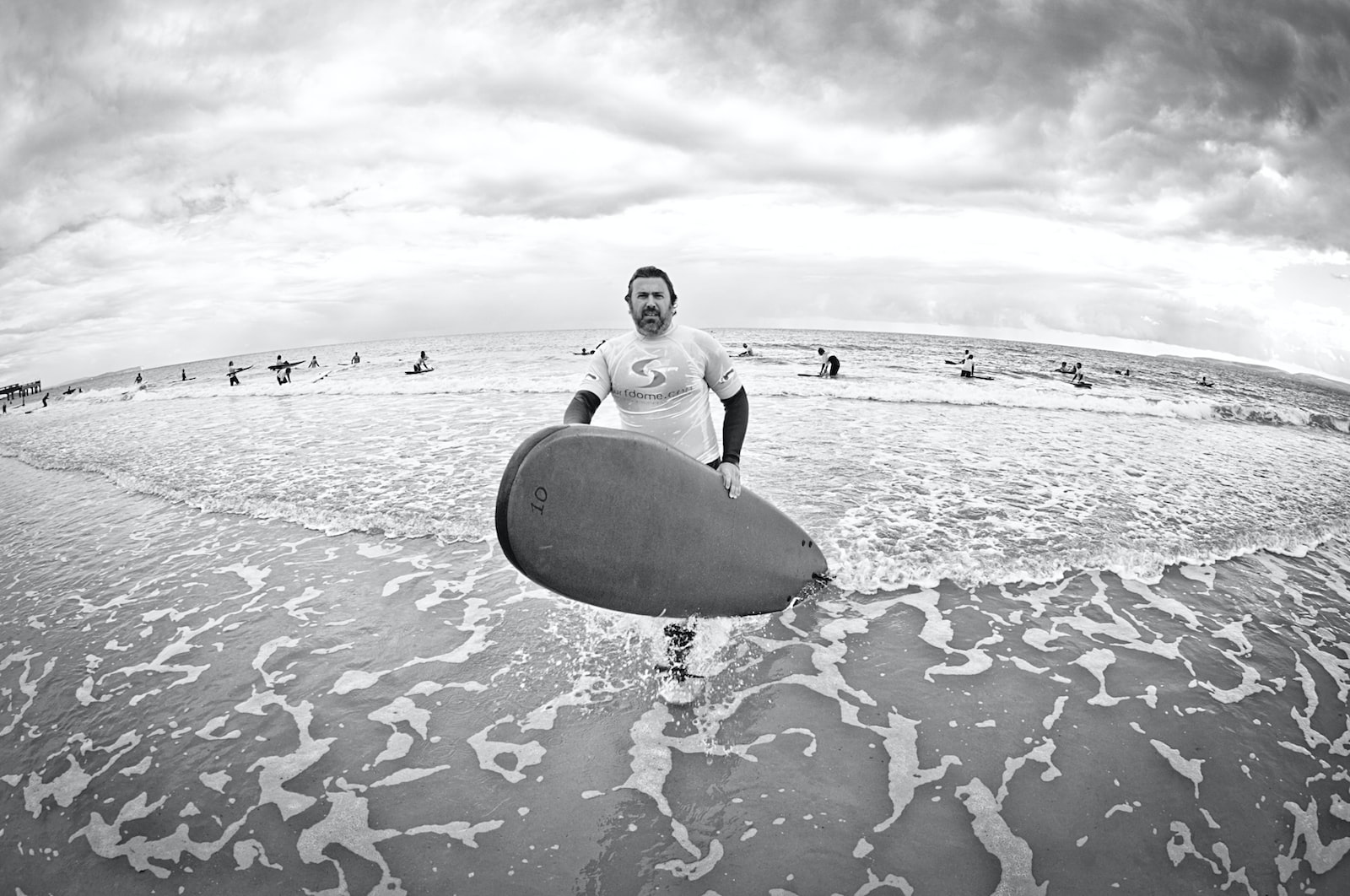 grayscale photo of man holding surfboard on beach